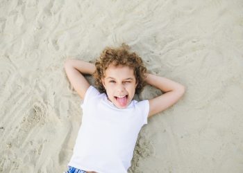 little curly blonde girl lies on the sand and smiles.summer portrait
